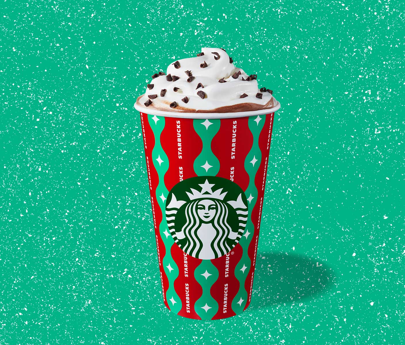 Hot espresso drink with whipped cream in a to-go cup with red and green stripes.