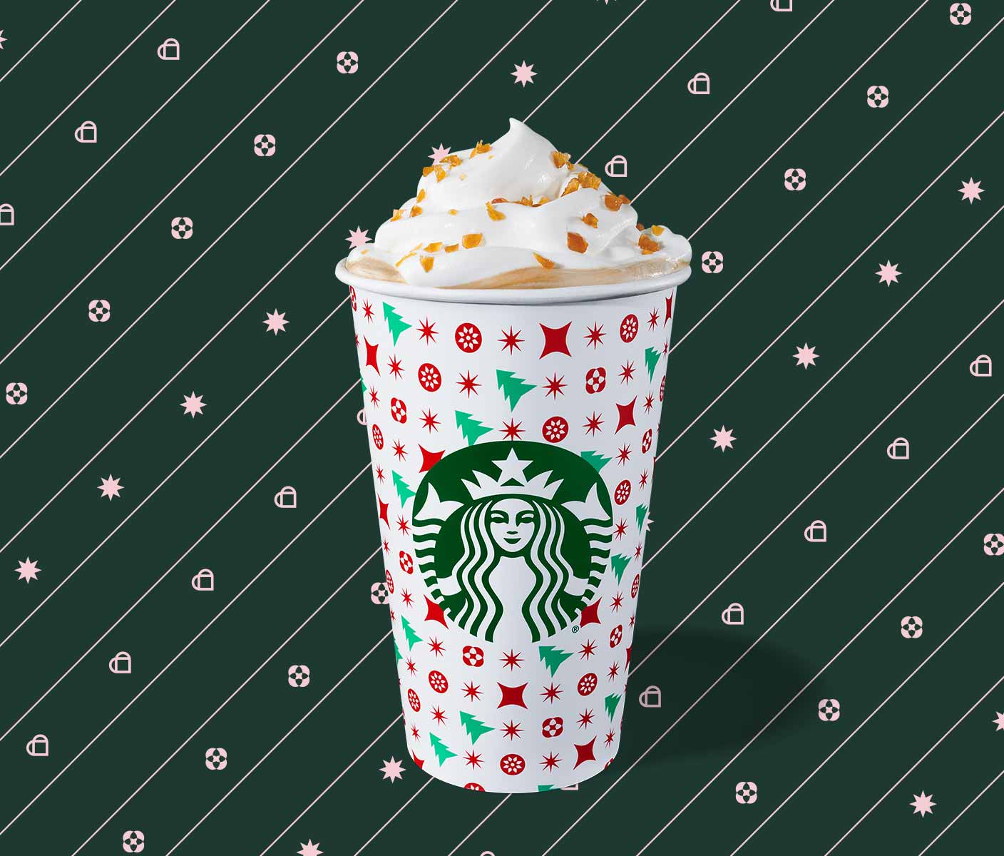 Hot espresso drink with whipped cream in a to-go cup with red stars and green trees on a white background.