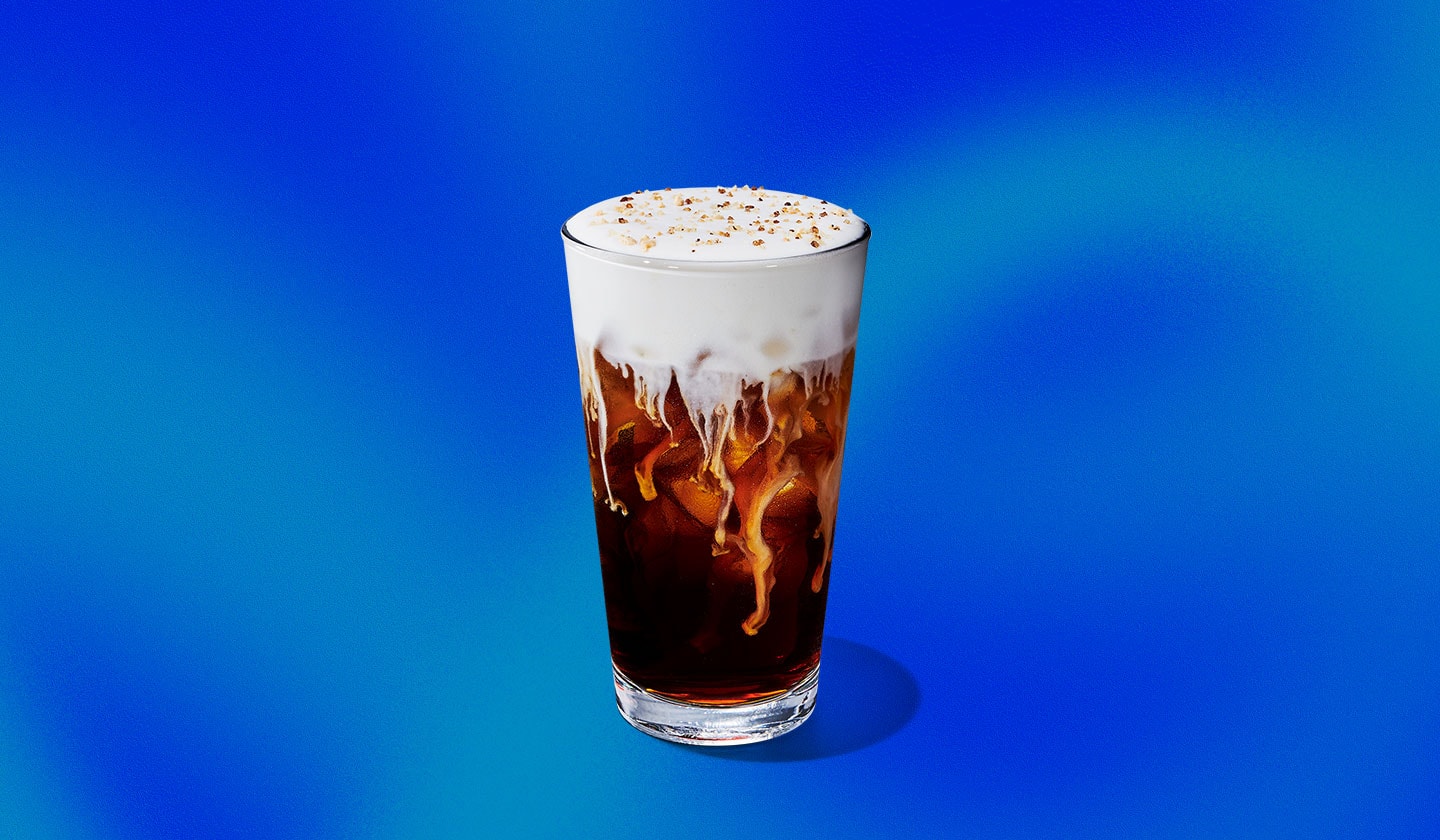 A cold coffee drink in a tall glass with a creamy topping and cookie crumbles.