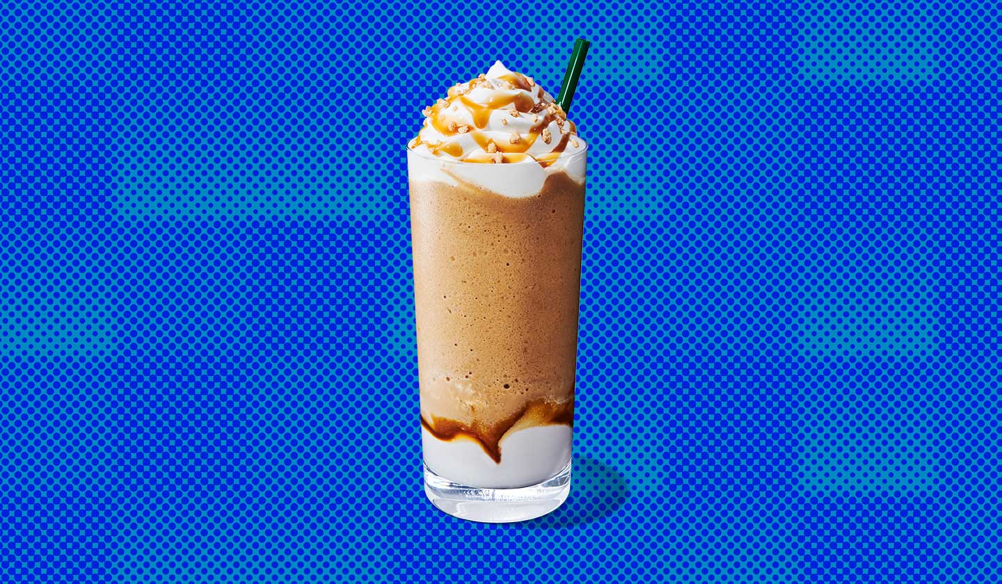 A blended coffee drink in a tall glass with whipped cream on top and a straw.