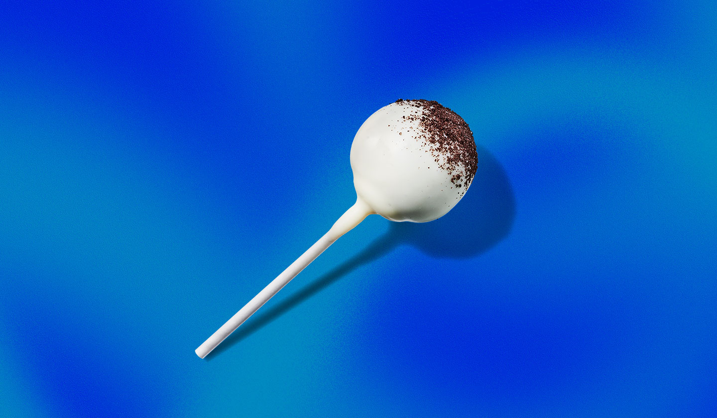 A cake pop with white frosting dusted with chocolate on top, laying on its side.