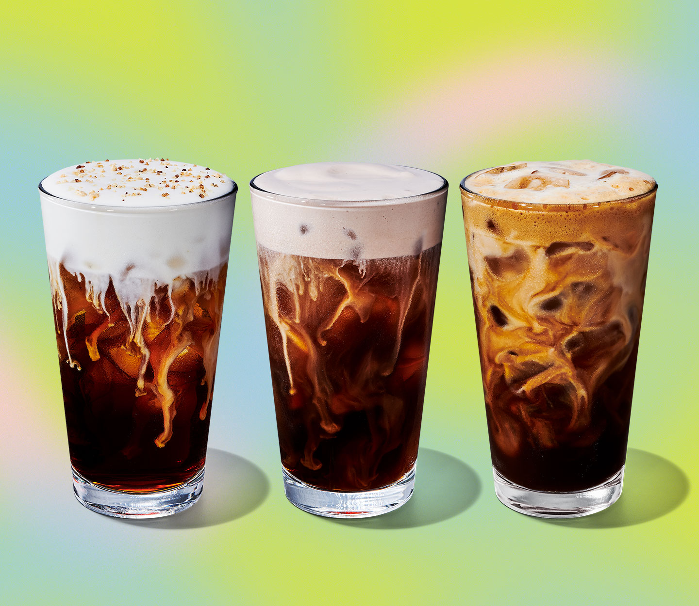 Three cold coffee drinks in tall glasses sitting side by side. The first two have a creamy topping and the third shows creaminess throughout the drink.