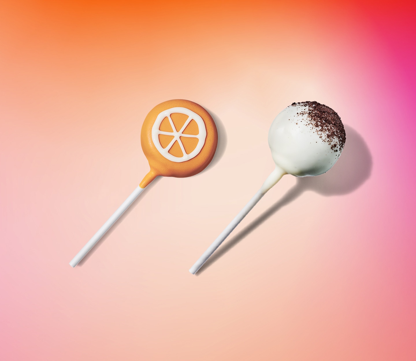 An orange cake pop with orange slices drawn in icing, a white cake pop with chocolate cookie crumbs.