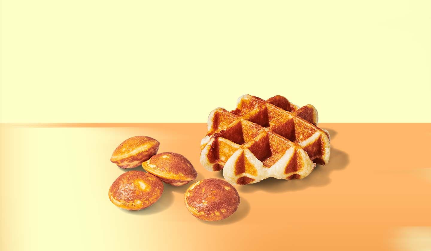 A golden brown waffle beside four golden brown mini pancakes against a warm yellow background featuring a rising sun.