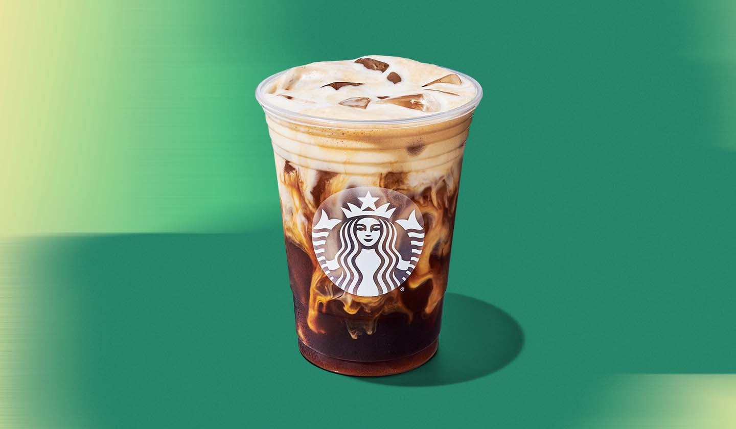 A transparent cold cup with frosted Starbucks siren featuring an iced coffee with cascading oat beverage and a frothy brown crema.