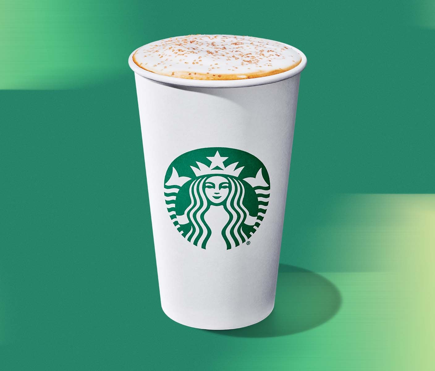 A white Starbucks hot cup with green siren with the lid off showing milky latte foam and a light brown butter topping.