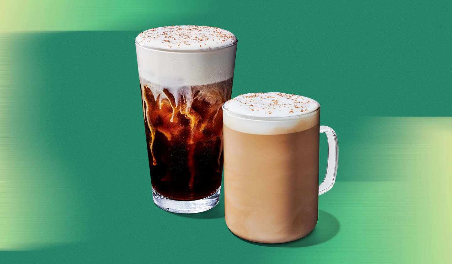 A cold brew with cold foam in a clear glass and a latte in a glass with a handle on a green textured background.