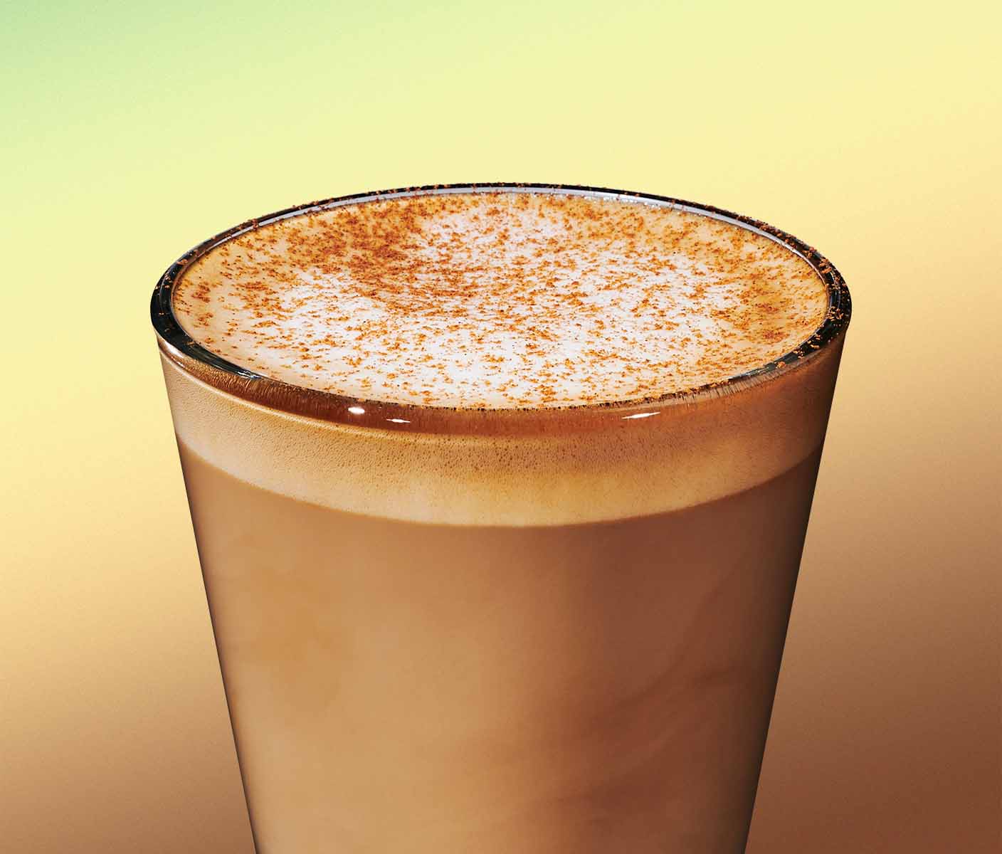 An espresso based beverage in glassware with brown sprinkles on the frothed top on a green background.