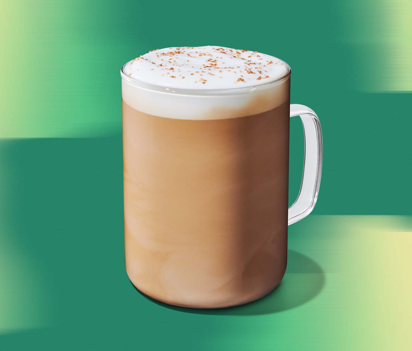 a latte in a glass with a handle on a green textured background.