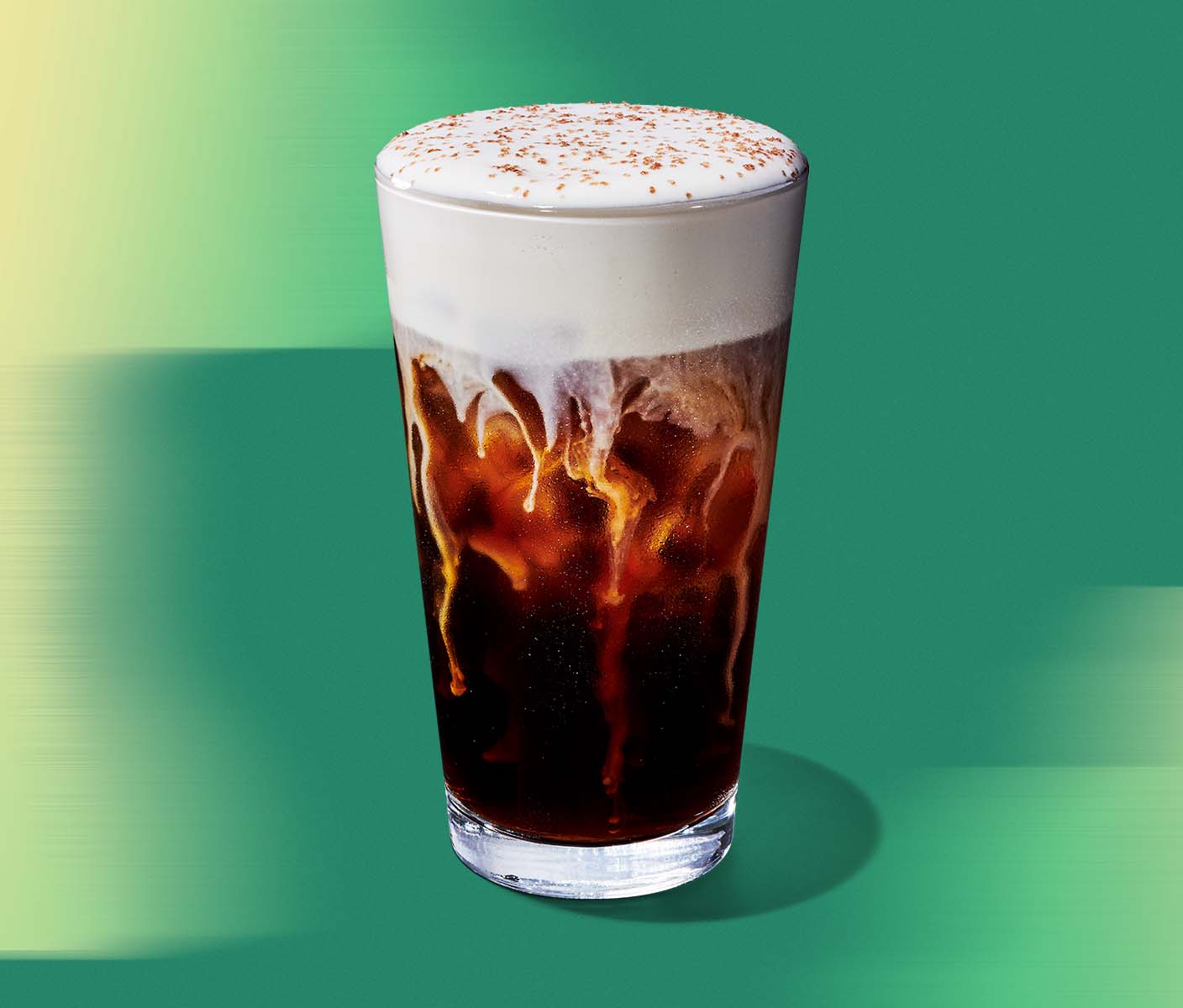 A cold brew with cold foam in a clear glass on a green textured background.