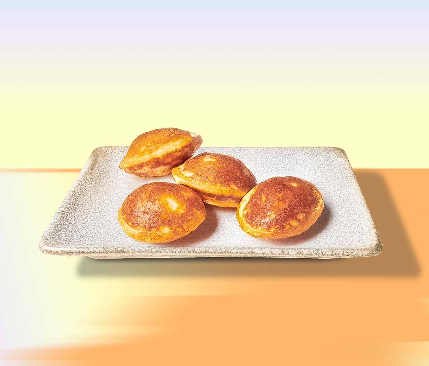 4 miniature pancakes on a rectangular plate. The background gradates from orange to yellow to blue.