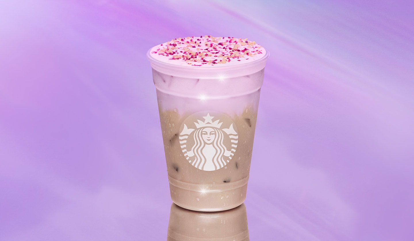 An iced tea beverage with a layer of light pink colored cold foam on a pink background.