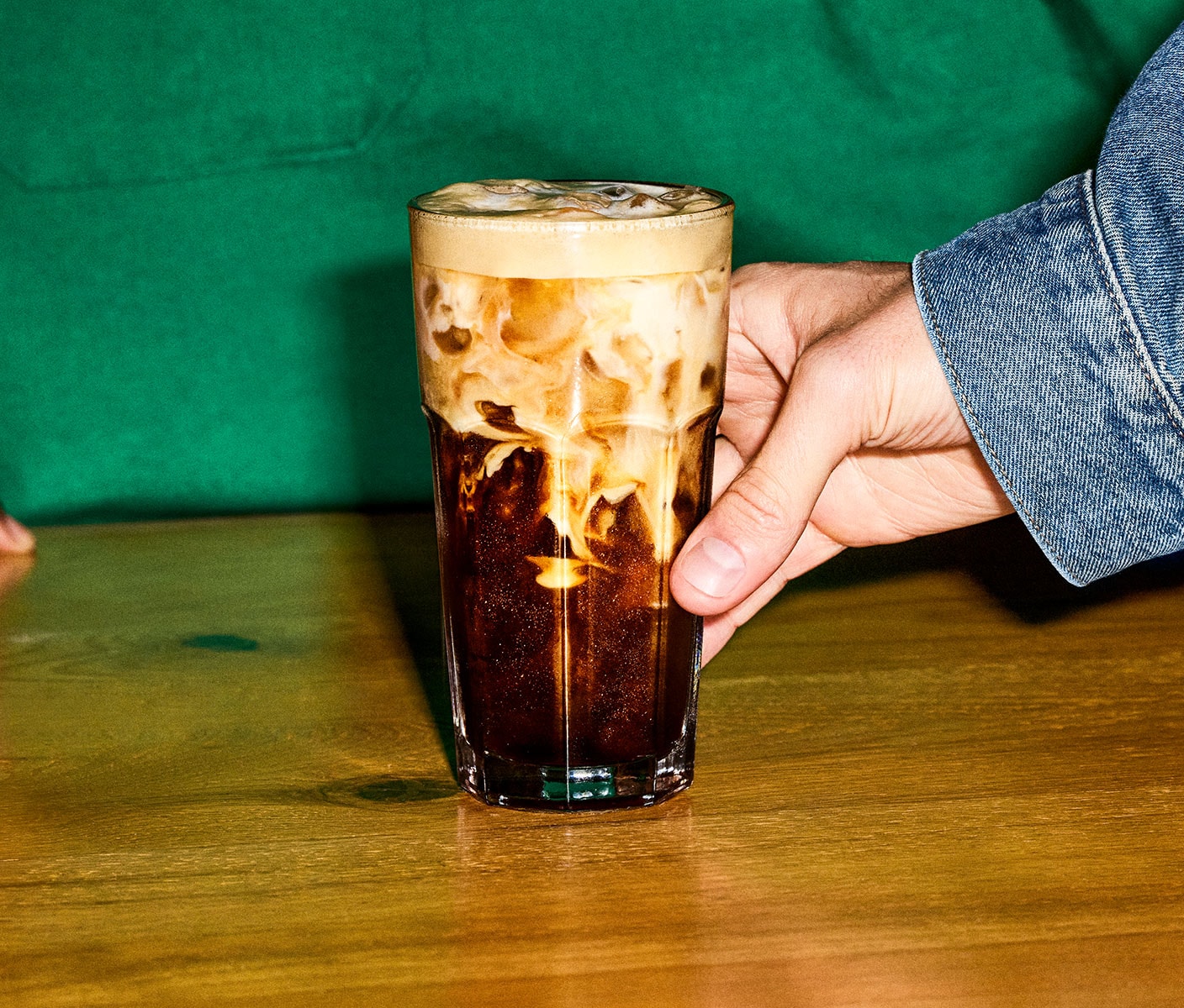 A customer is reaching for a handcrafted espresso beverage to enjoy for-here. A barista stands behind the counter.