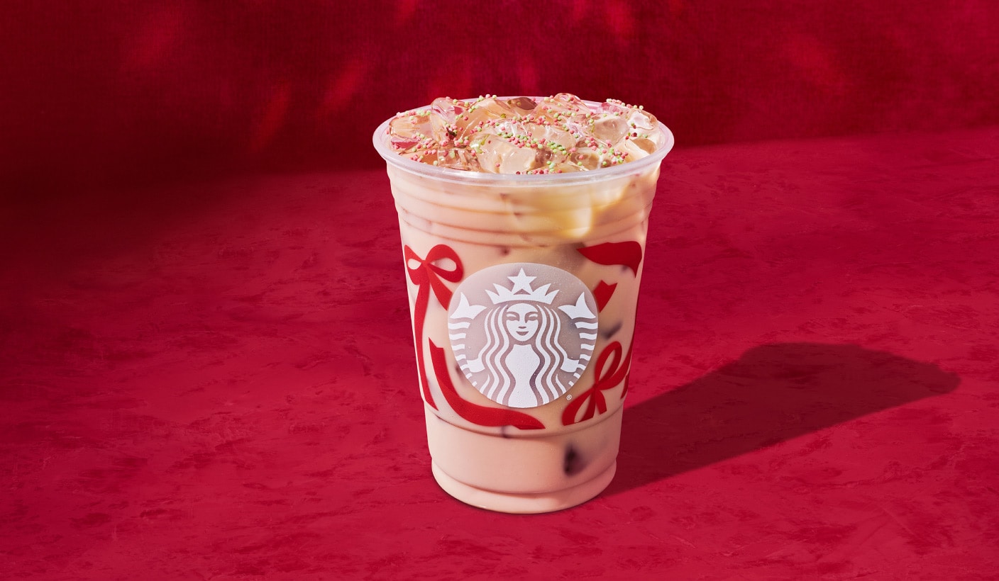 Une boisson glacée à base d’espresso dans une tasse des Fêtes, saupoudrée de paillettes rouges et vertes, sur fond rouge.