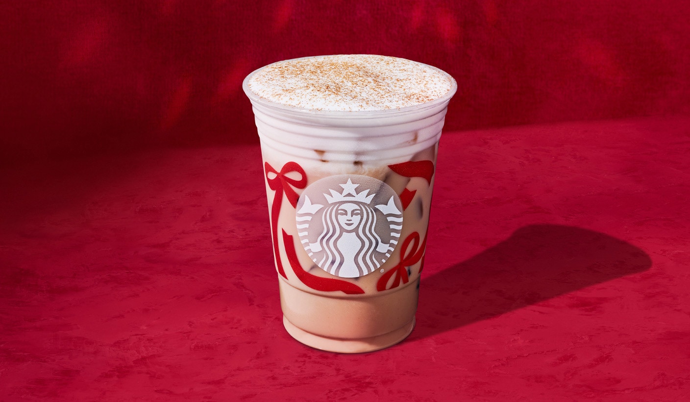 Une boisson glacée crémeuse au chai avec une garniture épicée sur un fond rouge vif.