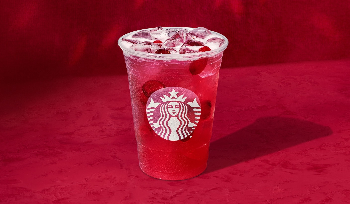 Une boisson glacée canneberge et orange aux couleurs éclatantes dans laquelle flotte des canneberges, sur un fond rouge vif.