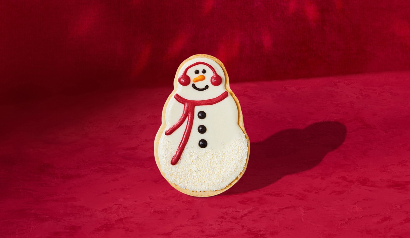 Un biscuit sablé en forme de bonhomme de neige finement détaillé sur un fond rouge.