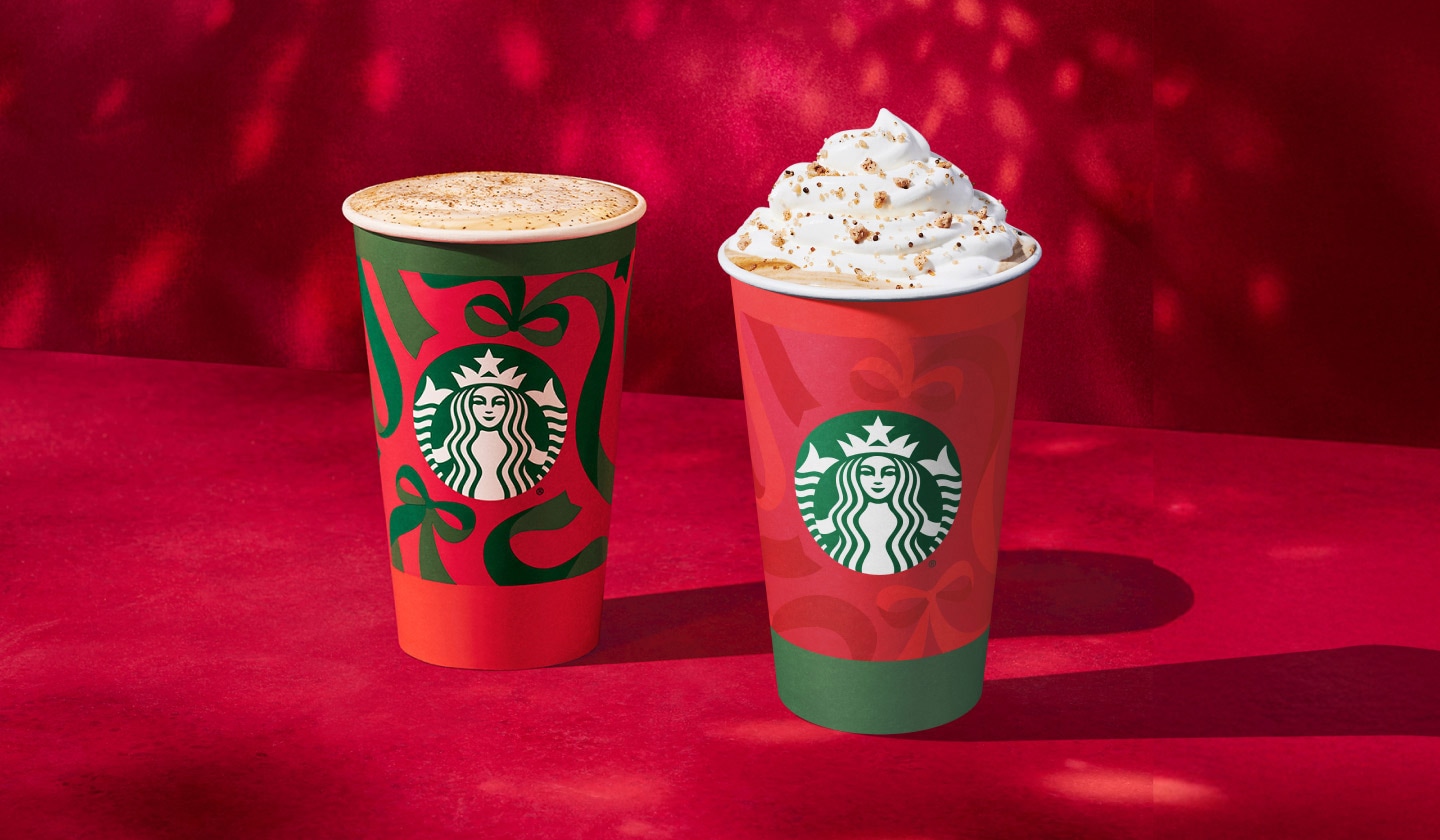 Deux boissons des Fêtes à base d’espresso sur un fond en velours rouge vif. À gauche, on voit une tasse rouge ornée de boucles vertes, nappée de lait vapeur onctueux saupoudré de muscade dorée. À droite, on voit une autre tasse rouge, ornée de boucles rouges et d’une bordure verte au bas de la tasse, coiffée de délicieuse crème fouettée, de lait vapeur et d’une garniture de marron doré.