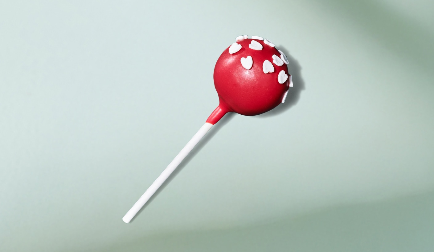 Un gâteau-suçon festif de couleur rouge vif décoré de bonbons en forme de cœur, sur un fond vert menthe.