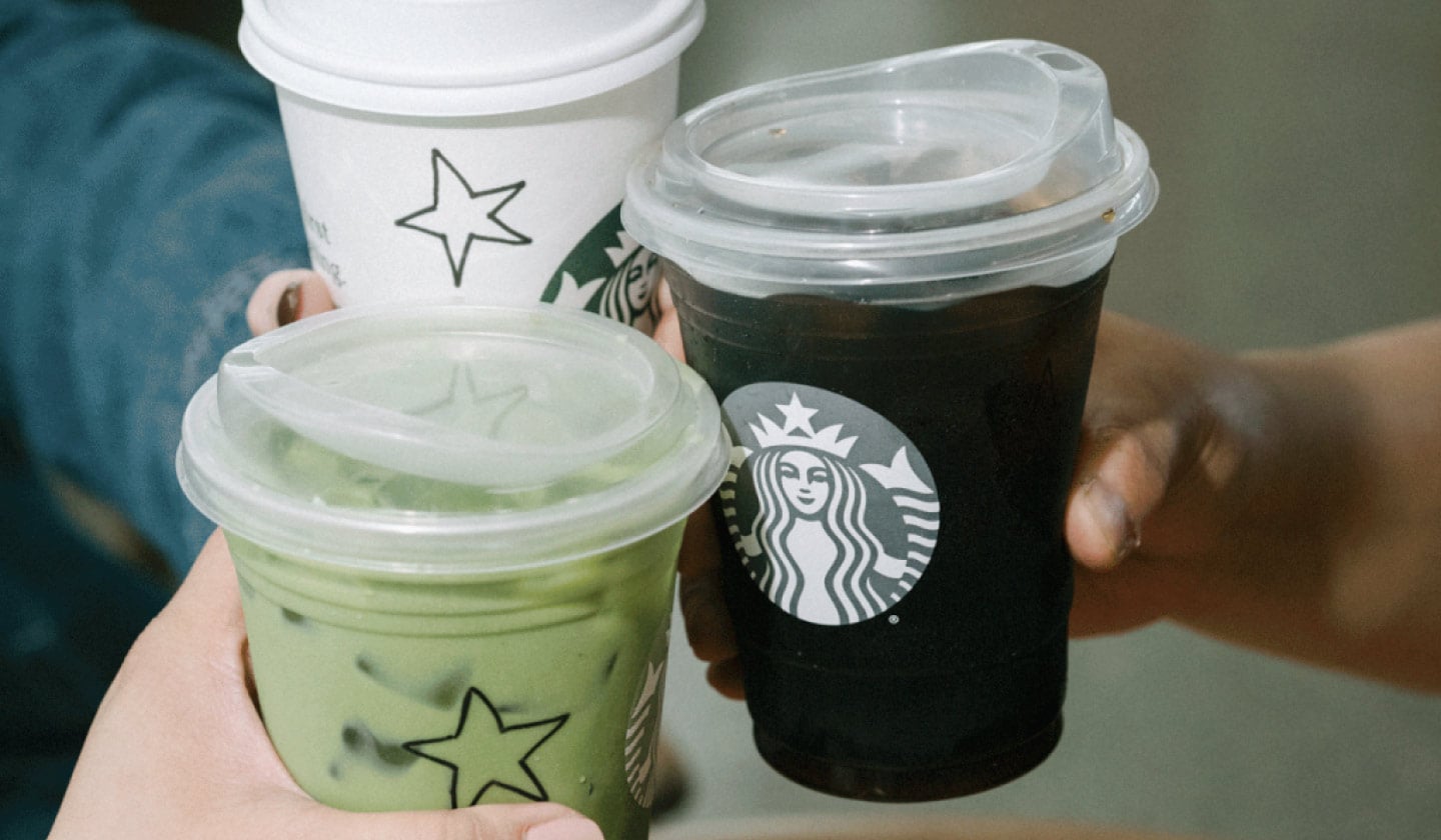Trois personnes trinquent avec leurs boissons Starbucks. Les tasses sont décorées à la main avec des étoiles.