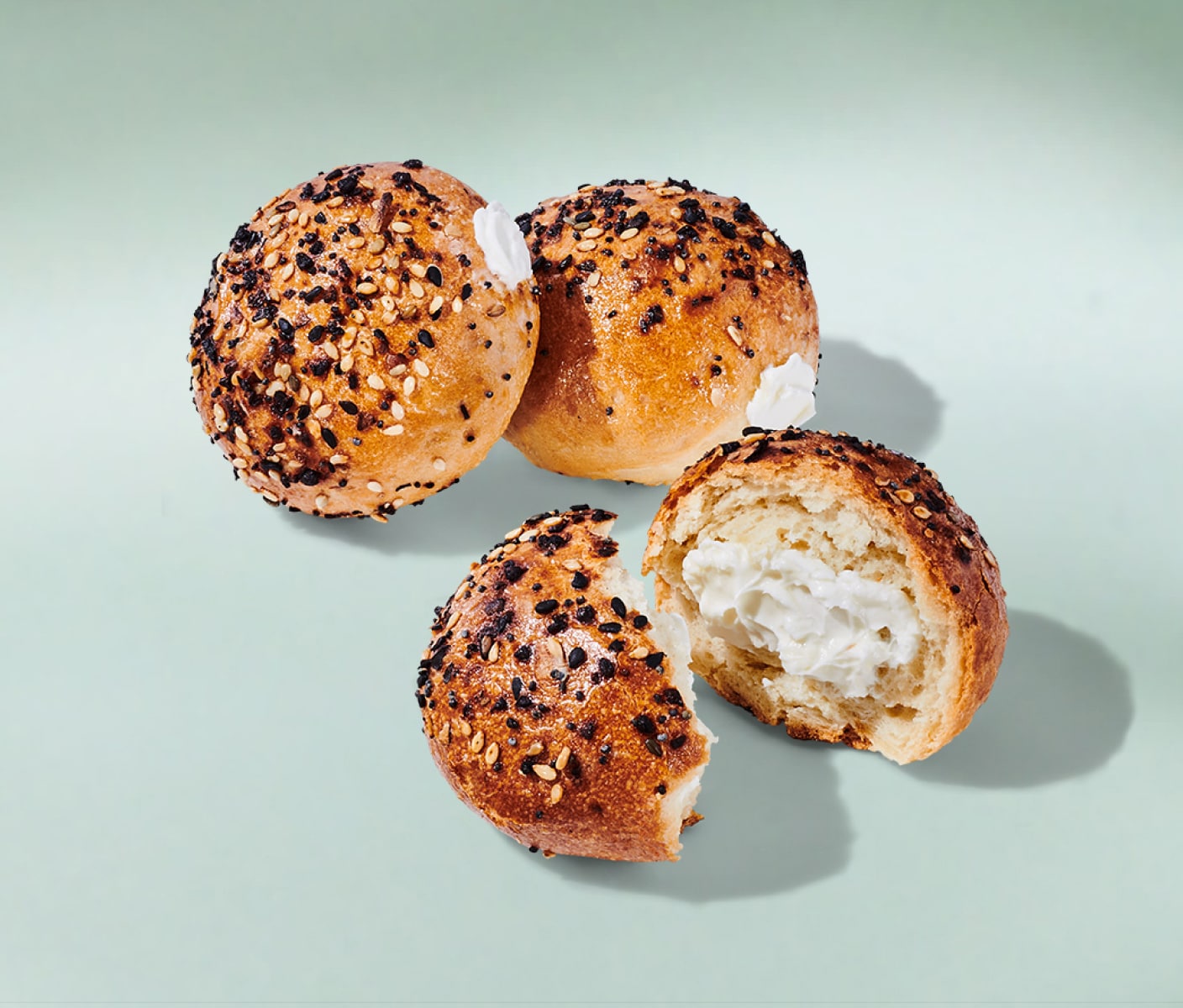 Trois petites bouchées de bagel, dont l’une est coupée en deux pour montrer le fromage à la crème qui se trouve à l’intérieur, sur un fond vert menthe.