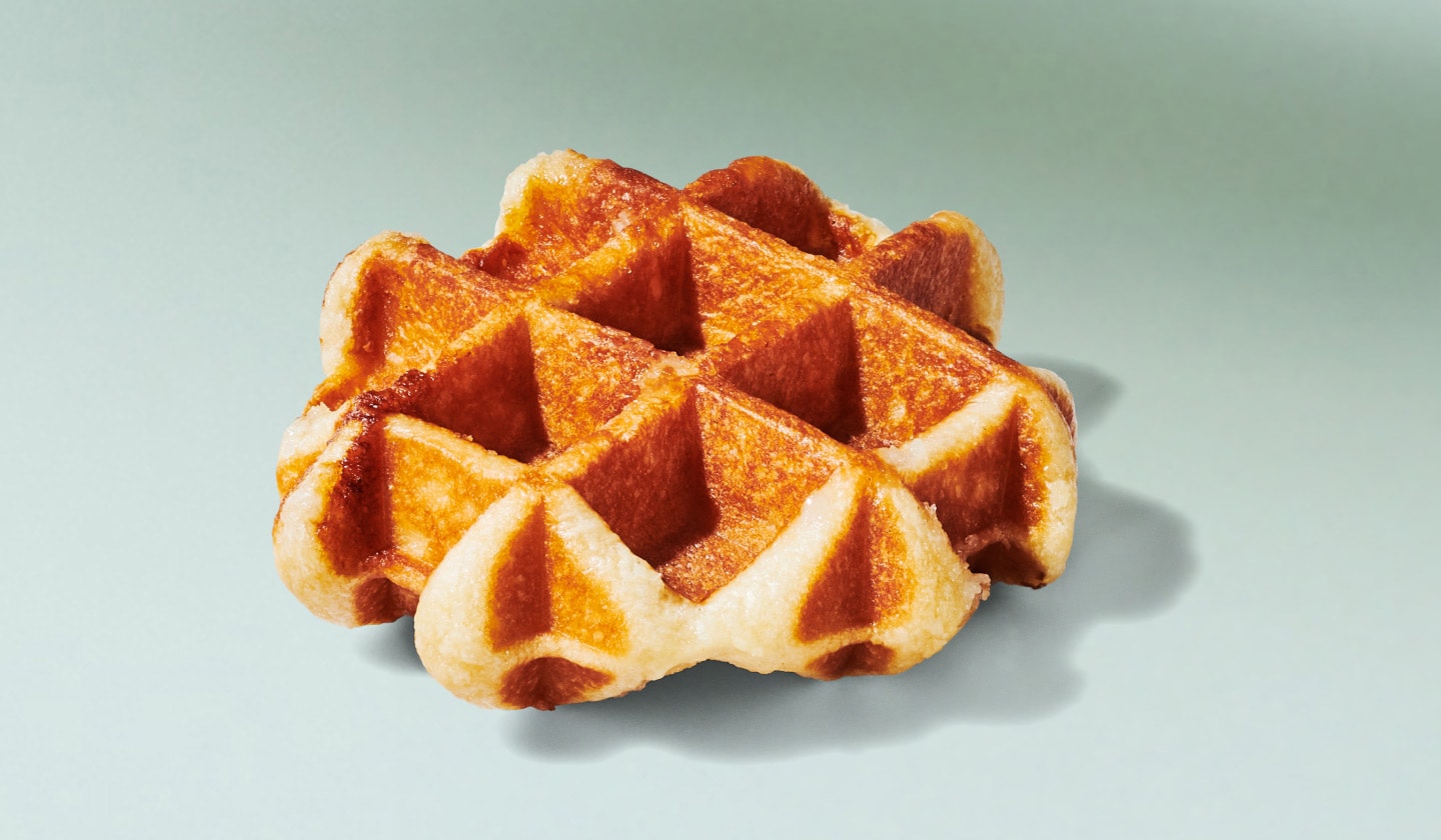 Une gaufre liégeoise dorée à la perfection, délicatement saupoudrée de sucre, est posée sur un fond vert pâle.