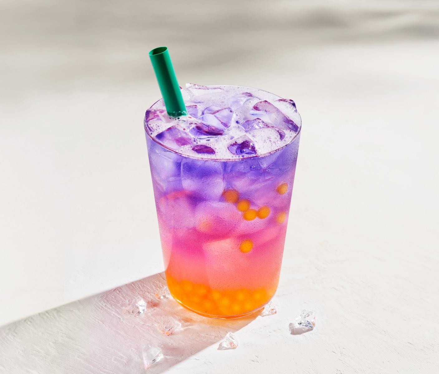 Une boisson rafraîchissante aux couleurs vives, garnie de perles tropicales, présentée sur un fond blanc ensoleillé.