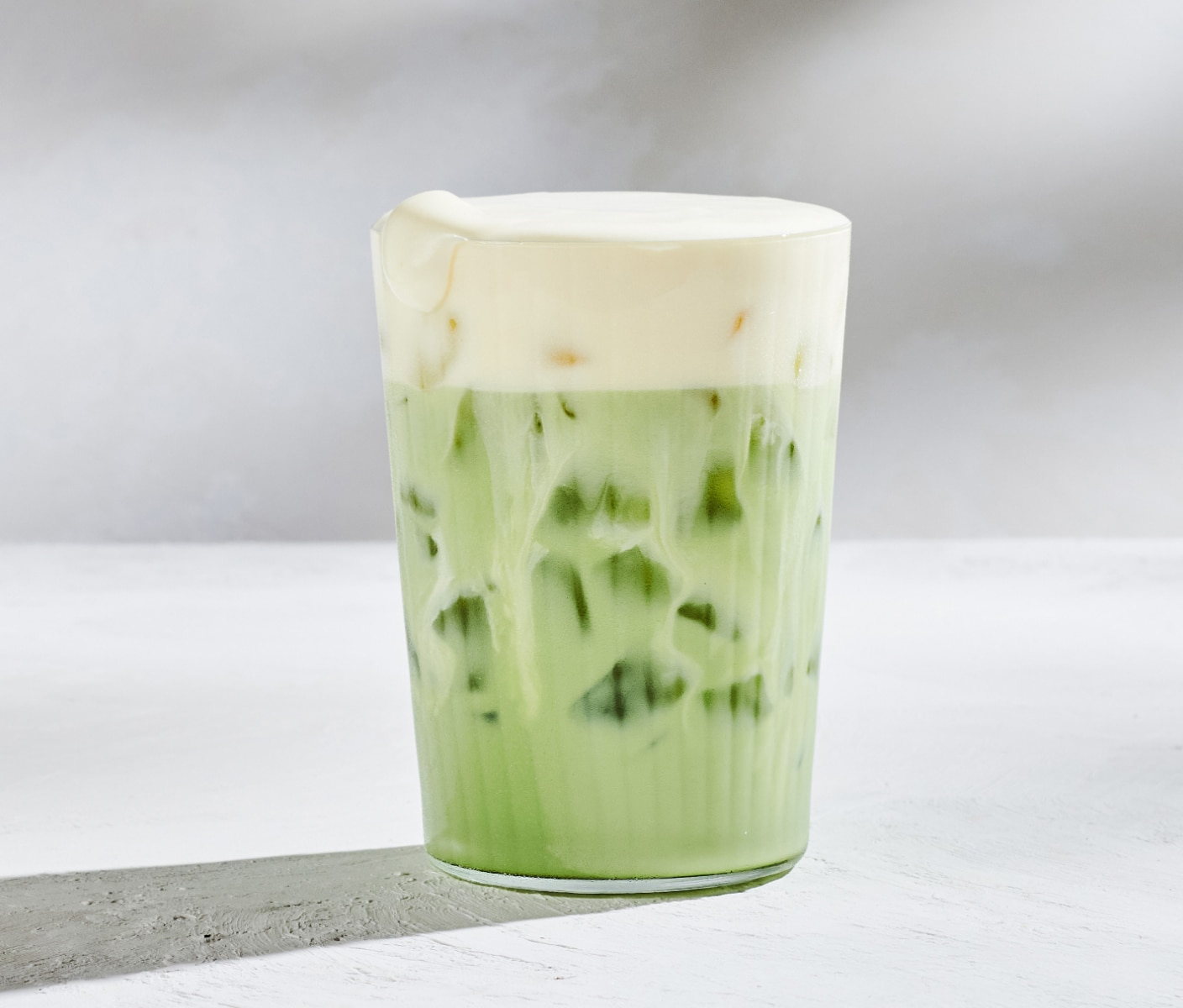 Un matcha glacé garni d’une mousse froide crémeuse à la mangue de couleur jaune.