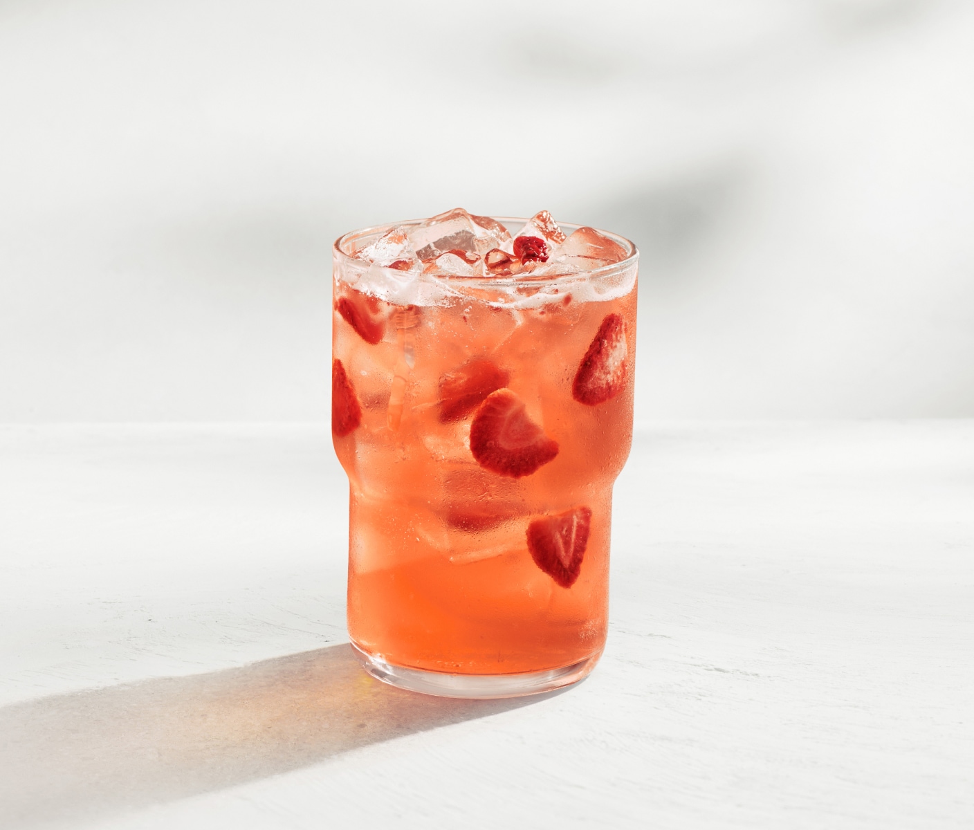 Un verre de boisson glacée rouge garnie de fraises séchées, présenté sur un fond beige.
