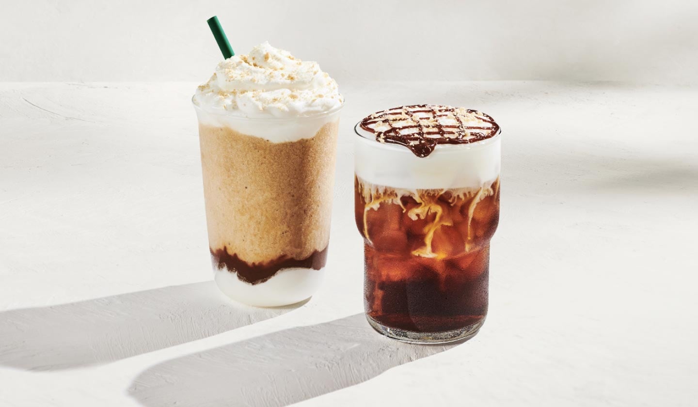 On voit deux boissons glacées : à gauche, un café frappé glacé dans lequel se superposent des couches de crème fouettée, de chocolat et de café frappé, couronné de crème fouettée et d’une garniture de biscuits Graham, avec une paille verte; à droite, un café infusé à froid dans un verre, coiffé de mousse froide crémeuse, d’un coulis de chocolat et de miettes de biscuits Graham.