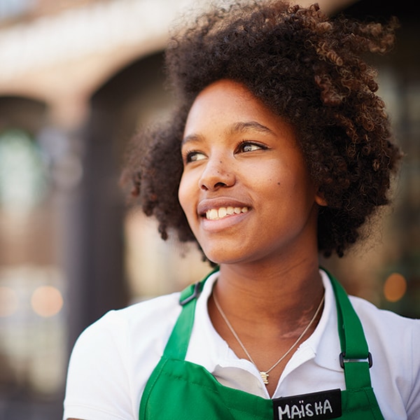 diverse female employee, wearing green apron, standing outside a Starbucks store