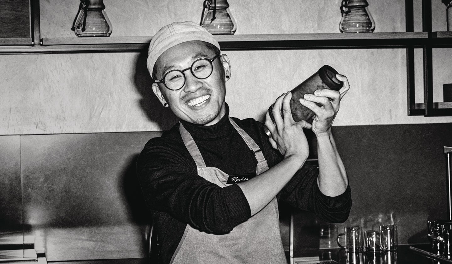 Un barista sympathique et accueillant prépare un café glacé avec enthousiasme derrière le comptoir.