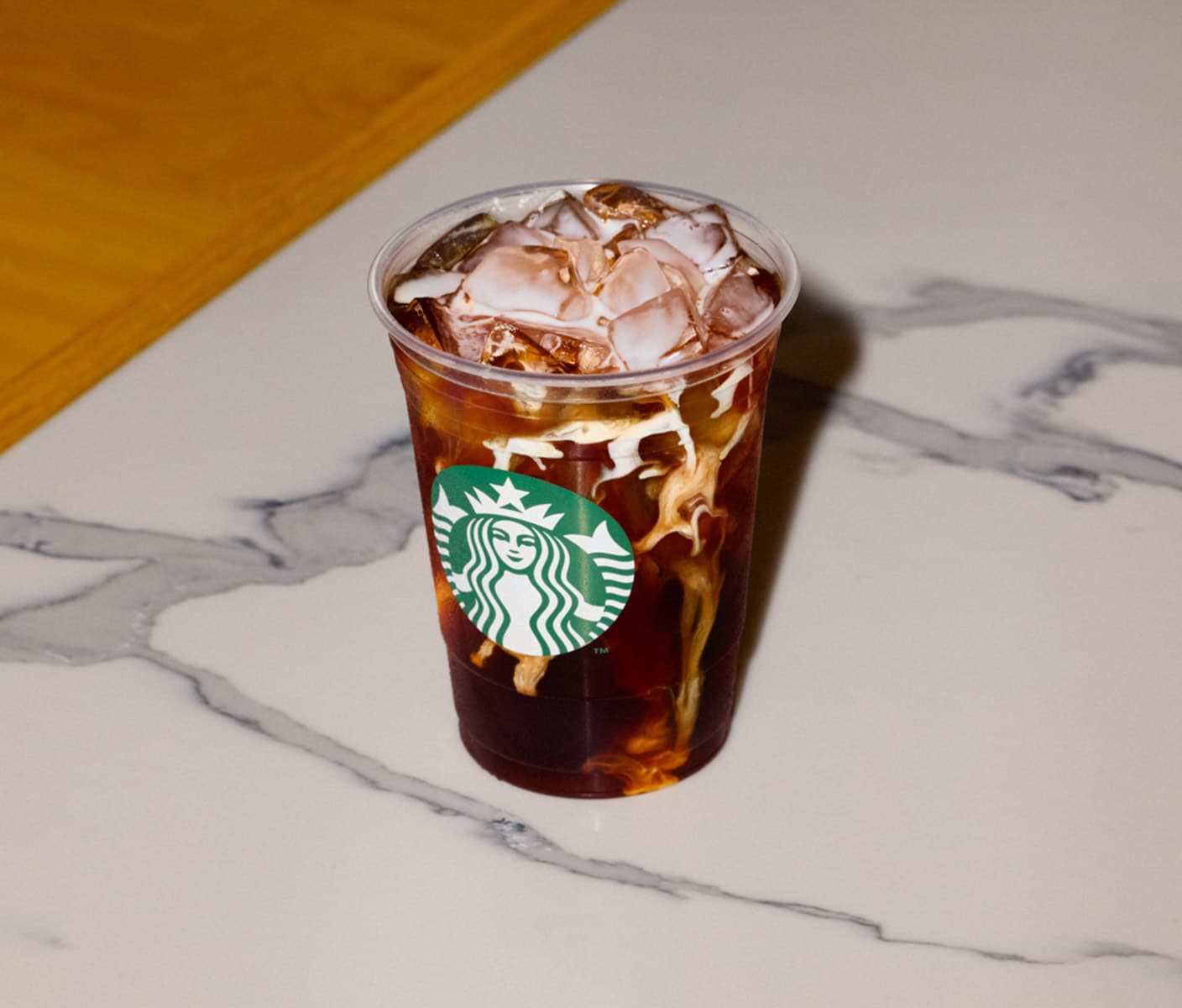 Un café glacé infusé à froid tourbillonne avec de la crème, créant un effet marbré. La tasse est posée sur un comptoir en marbre blanc veiné de gris.