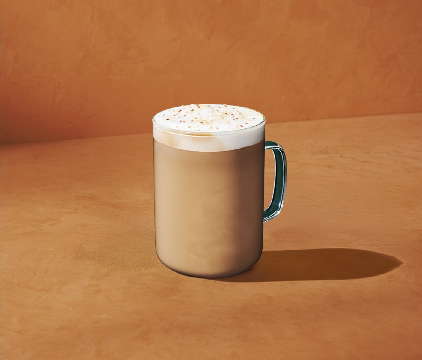Un délicieux latte chaud sur un fond orange chaleureux et saupoudré d’une garniture croquante aux pacanes.