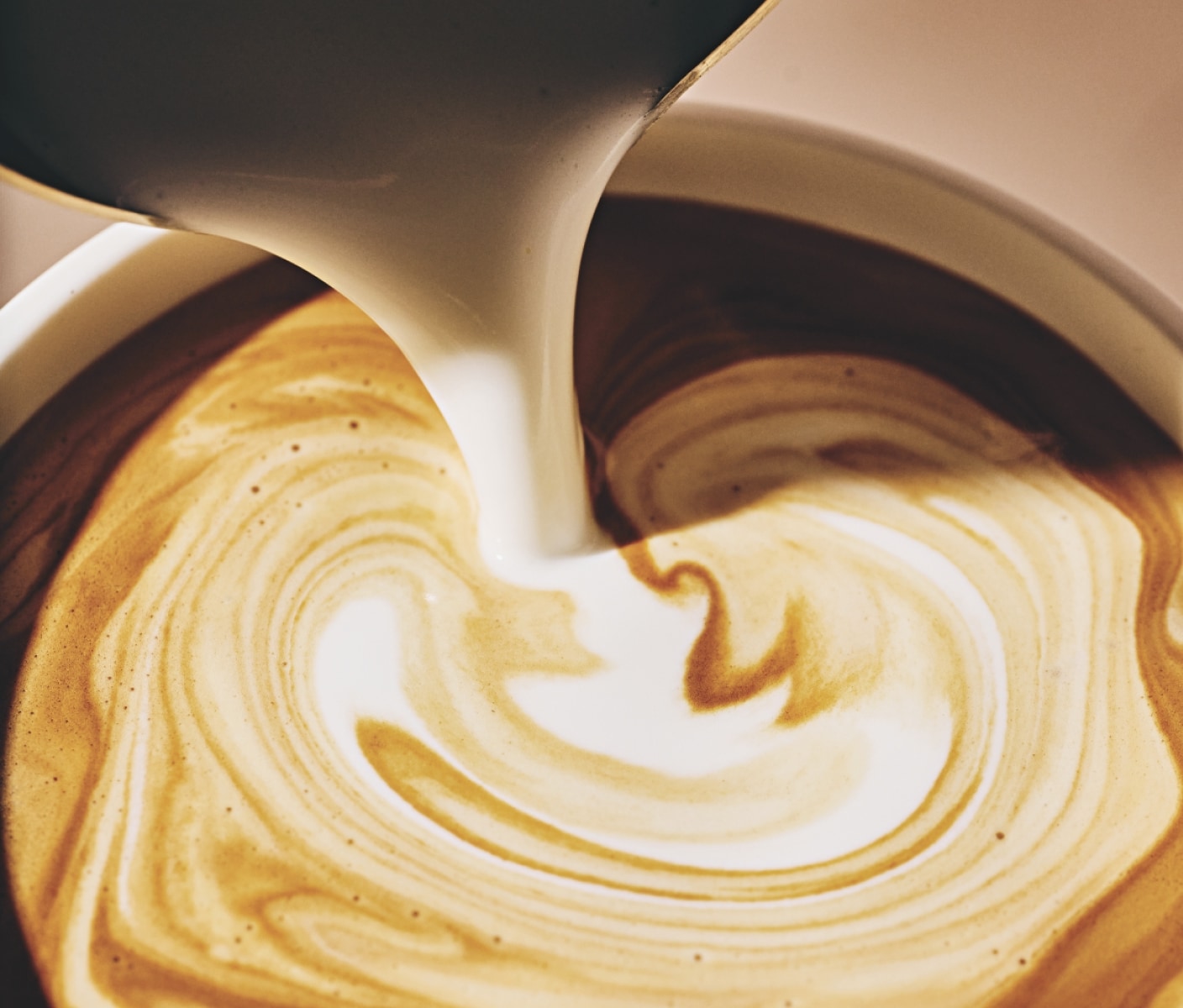 Gros plan en plongée sur un cortado, avec tourbillons d'espresso et de lait.